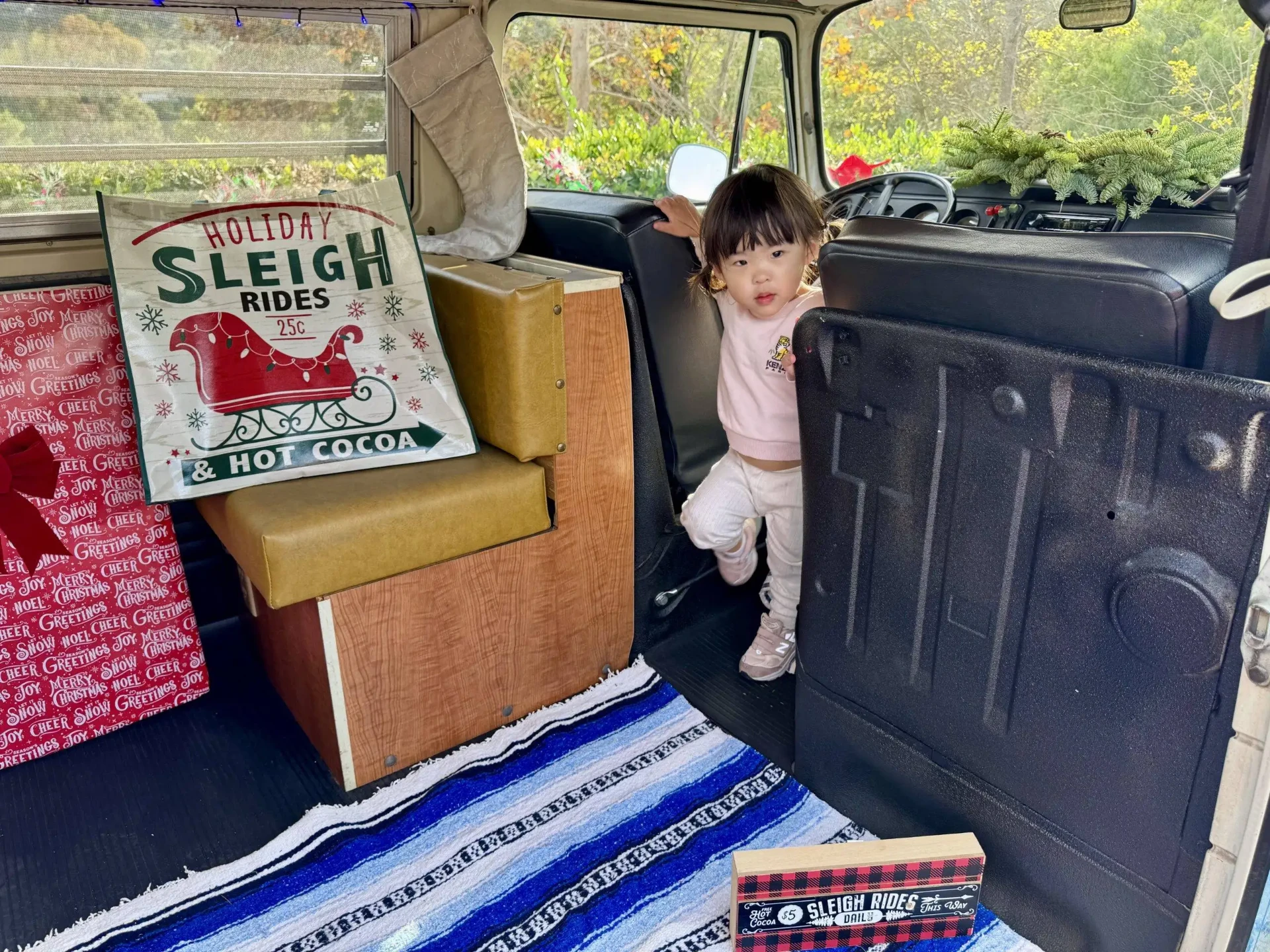 Toddler exploring the vintage interior of the Photobus with a holiday sleigh rides sign and woven blanket
