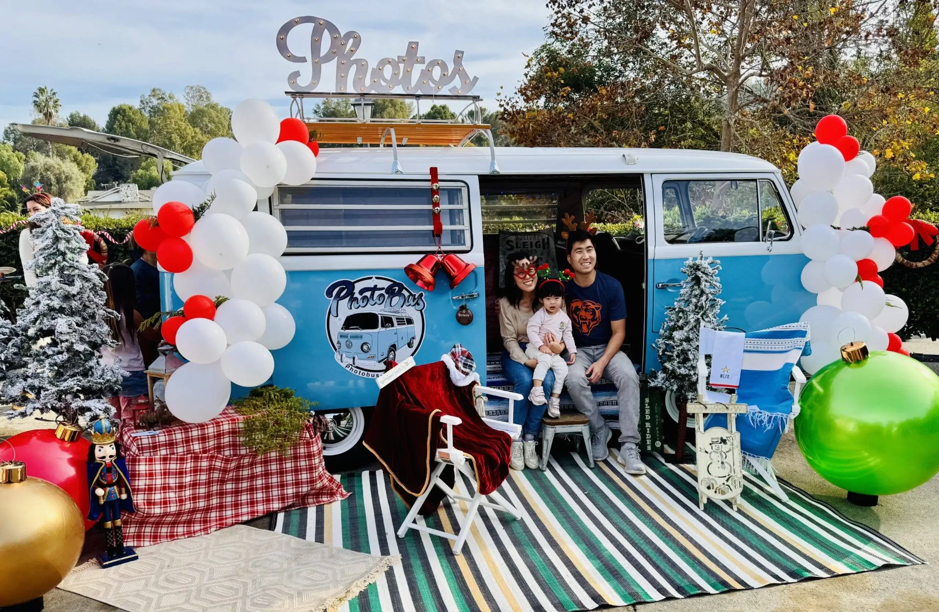 Family with a toddler posing inside the Photobus beneath the lit Photos marquee sign