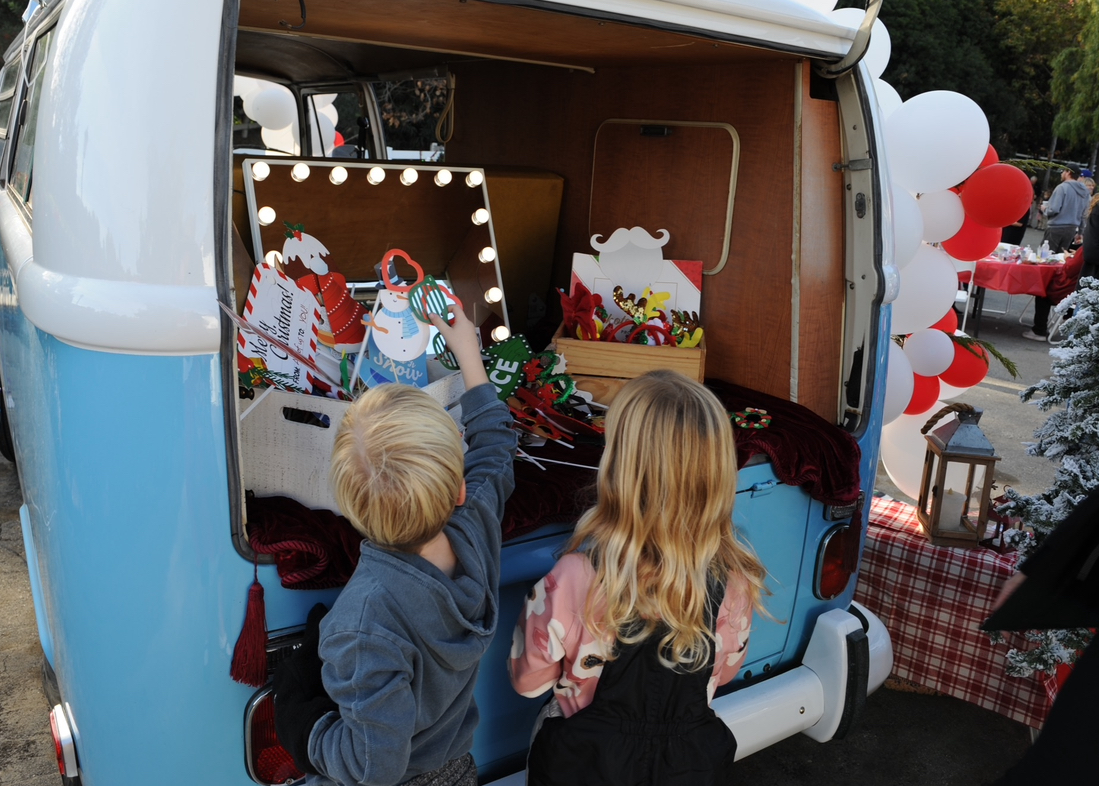 Two children reaching for props at the back of the Photobus beside a red and white balloon garland
