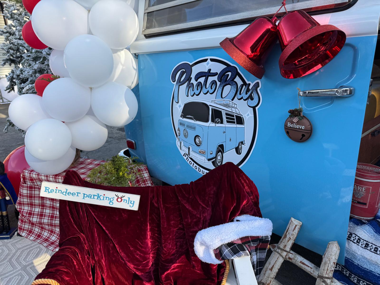 Close-up of the hand-lettered PhotoBus emblem on the sky blue bus with red holiday bells and a Reindeer Parking Only sign