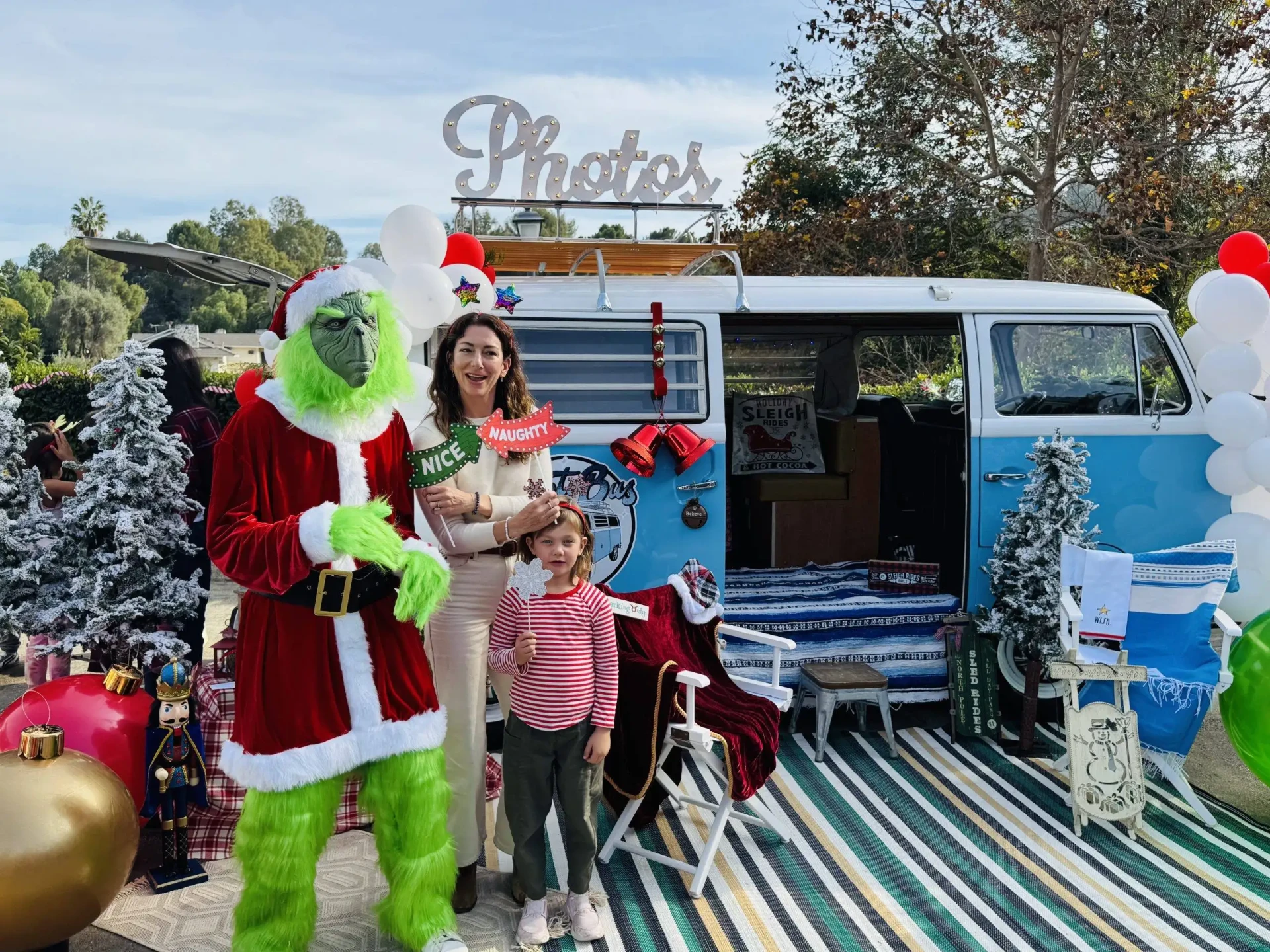 Guests posing with a costumed holiday character in front of the Photobus at a community event