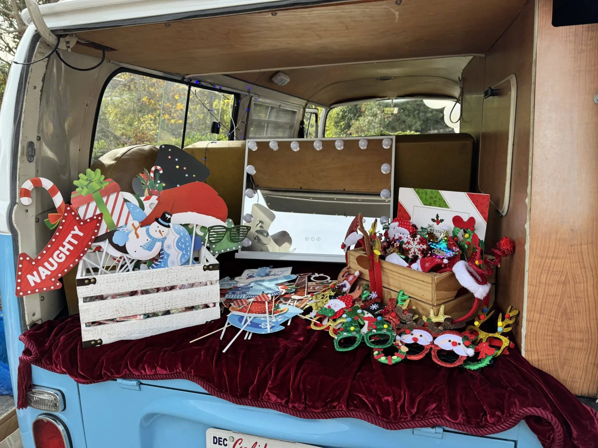 Photo booth prop table inside the Photobus with a lighted vanity mirror, crates of props and holiday glasses