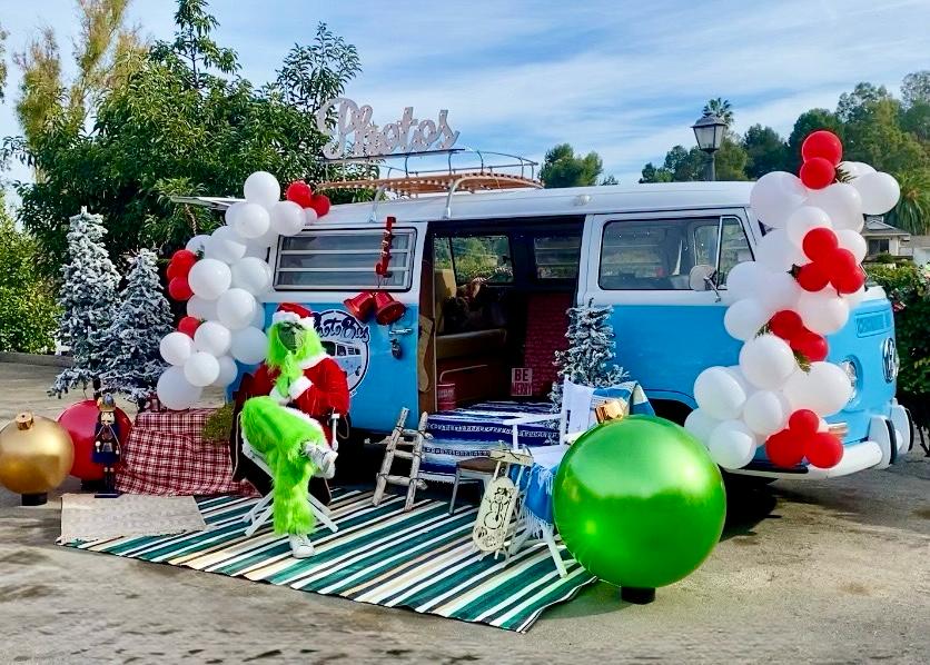 Holiday Photobus scene with a costumed green character in a director's chair, striped rug and oversized ornaments
