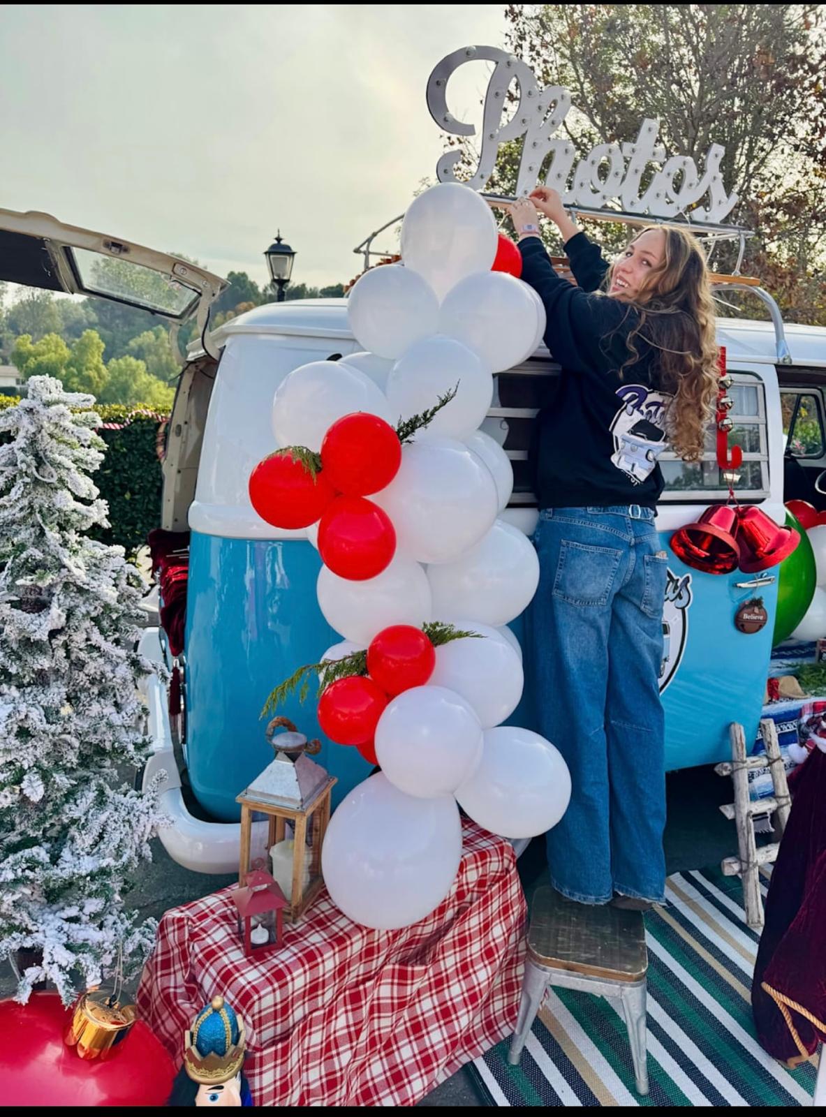 Photobus attendant on a step stool hanging the lit Photos marquee sign above the balloon garland
