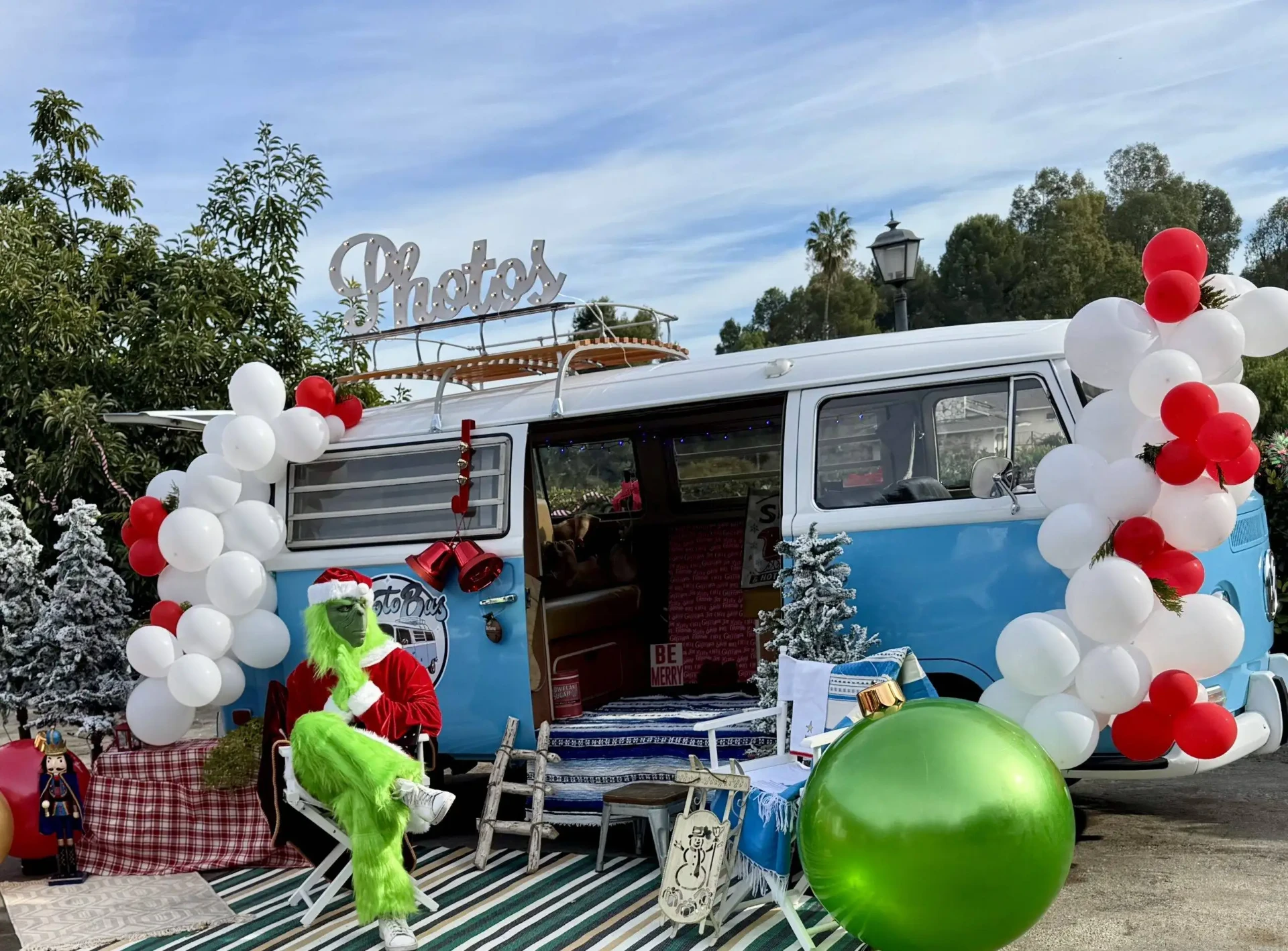 Costumed holiday character lounging in a director's chair in front of the decorated Photobus