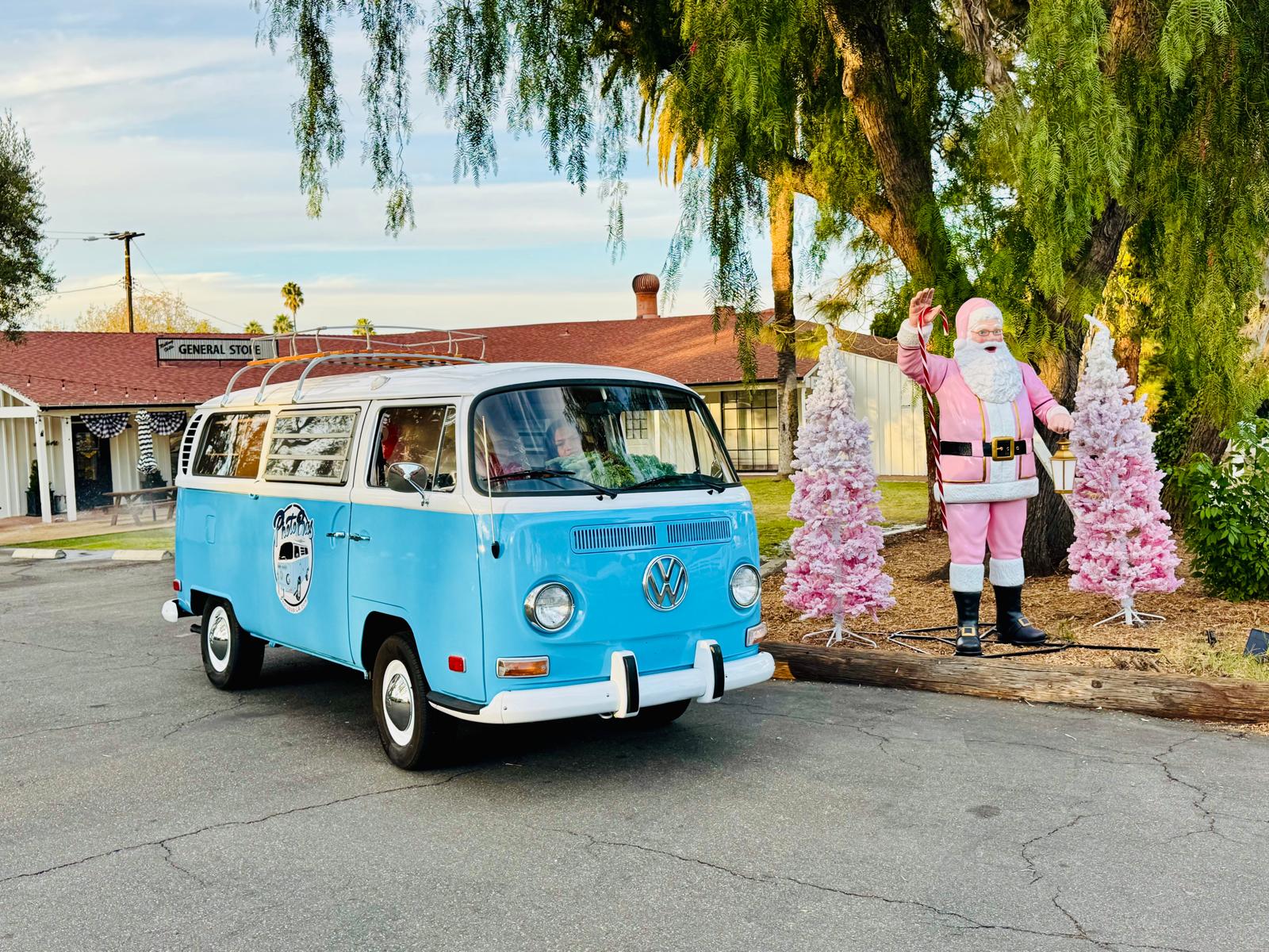 Front view of the VW Photobus parked on a ranch driveway beside a pink Santa and flocked trees